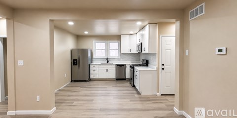 A kitchen with white cabinets and a refrigerator in a room with wooden floors.