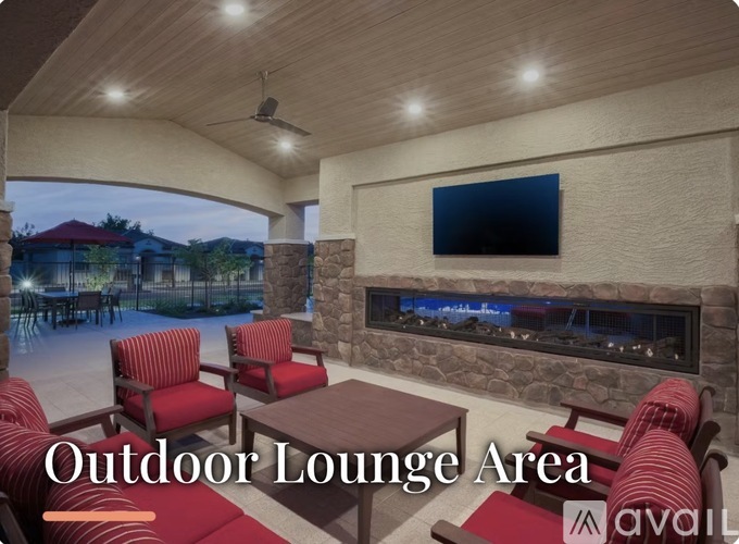 A cozy outdoor lounge area with red chairs and a stone fireplace.