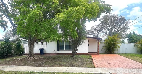 A white house with a tree in front and a red brick pathway leading to the front door.
