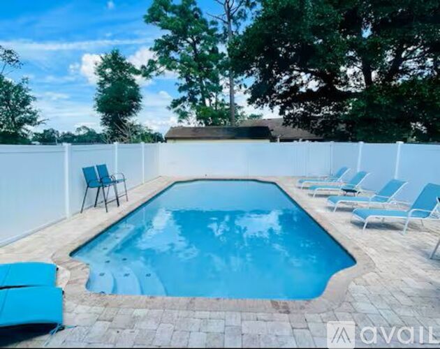 A pool surrounded by a white fence and blue lounge chairs.