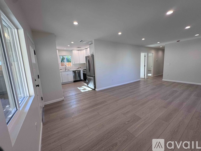 A spacious room with wooden flooring and a kitchen area in the background.