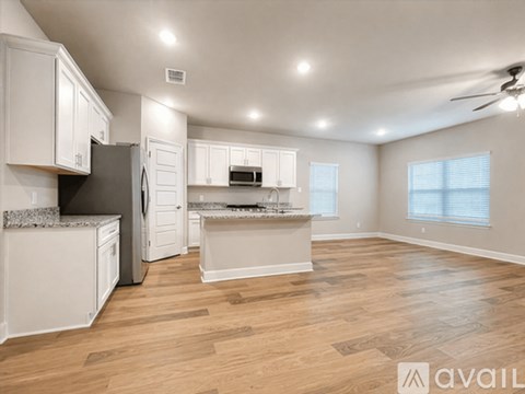 A spacious kitchen with white cabinets and a wooden floor.