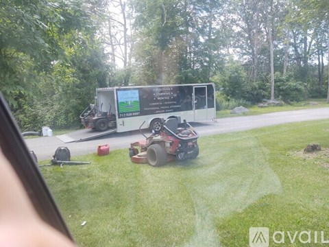 A lawnmower is cutting grass in front of a bus.