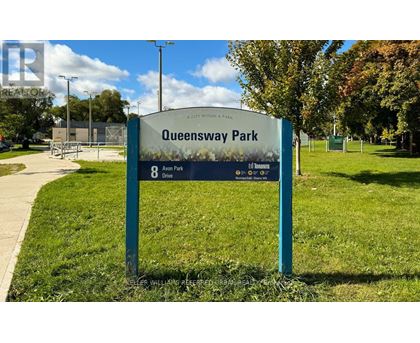 A sign for Queensway Park is displayed in front of a grassy area.