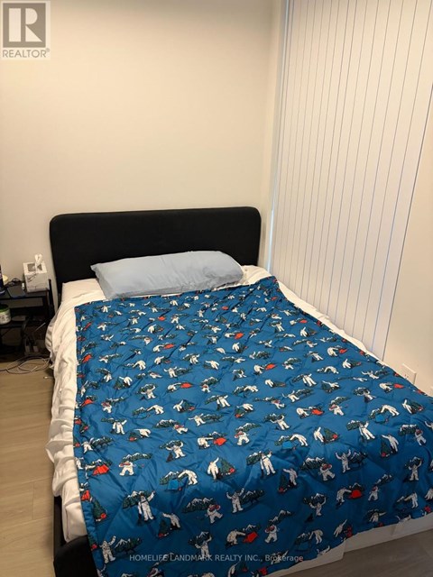 A bed with a blue dinosaur print sheet is in a room with a white wall.