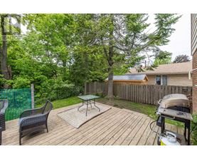 A backyard with a wooden deck, a grill, and a green fence.