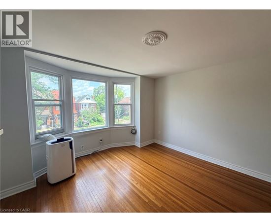 A room with wooden floors and a window overlooking a residential area.