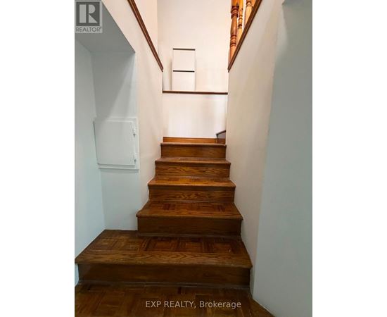 A set of wooden stairs with a white wall and a brown wooden handrail.