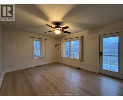 A room with a ceiling fan and two windows.