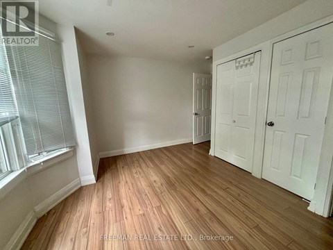 A room with wooden flooring and white walls, with a window on the left and a door on the right.