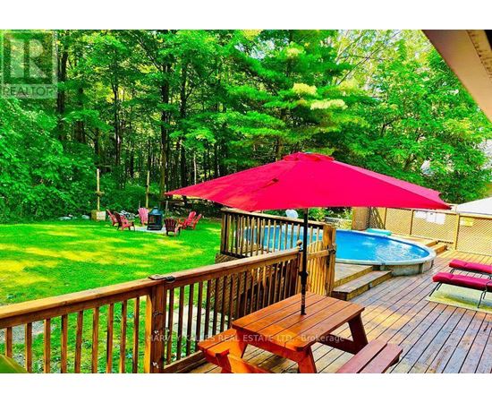 A red umbrella is on a wooden deck overlooking a pool.