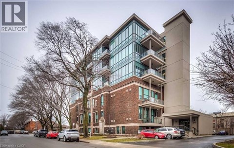 A modern building with a glass facade and a brick base is surrounded by parked cars.