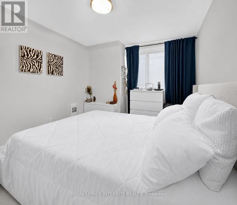 A bedroom with a white bed and a window with blue curtains.