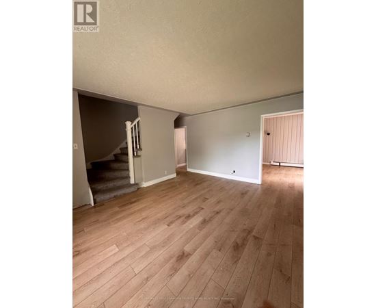 A room with wooden flooring and a staircase leading to another room.