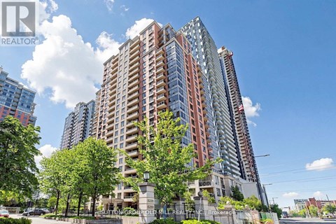 A tall residential building with a red and white facade stands in front of a blue sky with clouds.