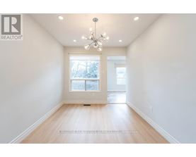 A well-lit, empty room with a chandelier and a window with a view of trees outside.