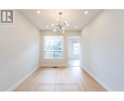 A well-lit, empty room with a chandelier and a window with a view of trees outside.