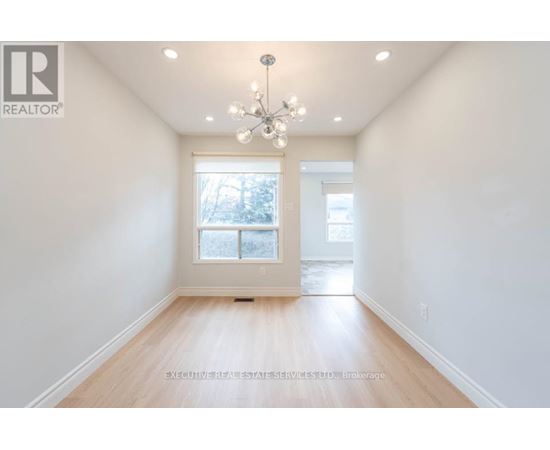 A well-lit, empty room with a chandelier and a window with a view of trees outside.