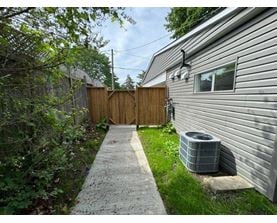 A concrete walkway leads to a wooden fence and a house with a grey siding.