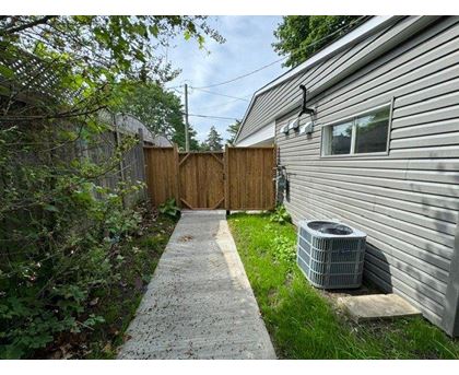 A concrete walkway leads to a wooden fence and a house with a grey siding.