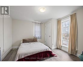 A bedroom with a bed, a window with curtains, and a wooden floor.