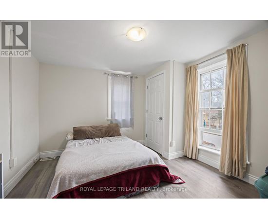 A bedroom with a bed, a window with curtains, and a wooden floor.