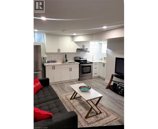 A modern kitchen with white cabinets and a black couch with red pillows.