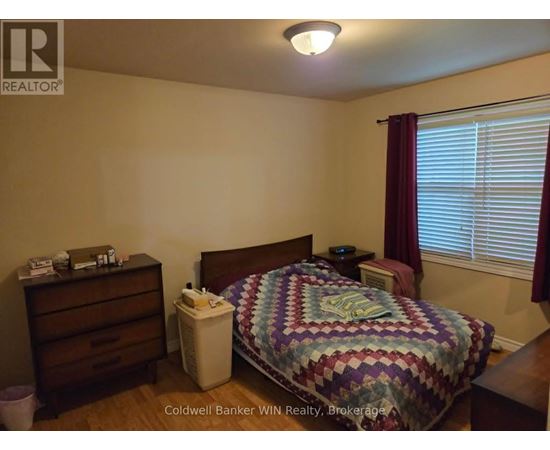 A bedroom with a bed, nightstand, and window with blinds.
