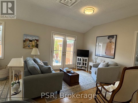 A living room with a grey couch and a painting of a woman on the wall.