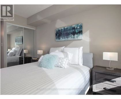 A bedroom with a large bed, a nightstand with a lamp, and a painting on the wall.