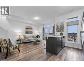 A well-lit, spacious living room with a striped armchair and a kitchen area with a refrigerator and sink.
