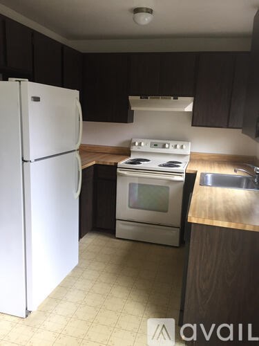 A white refrigerator stands in a kitchen with a stove and sink.