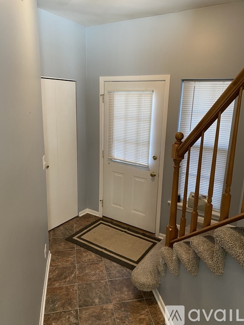 A hallway with a white door, brown stairs, and a rug on the floor.