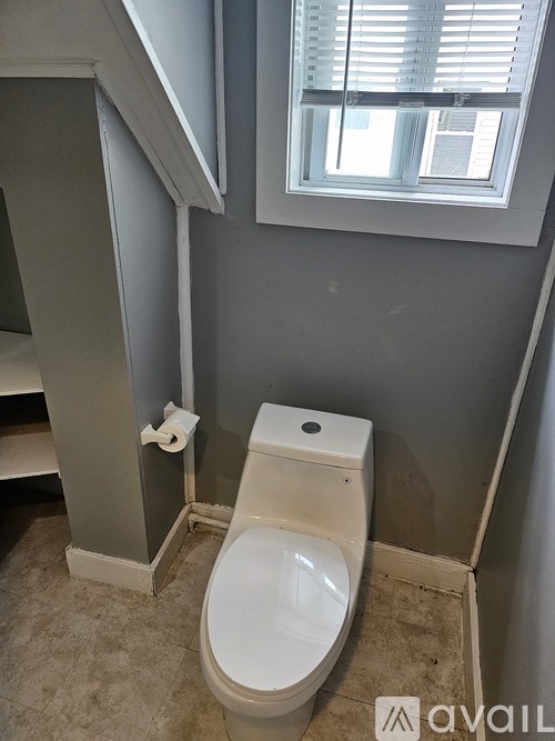 A white toilet in a bathroom with a window above it.