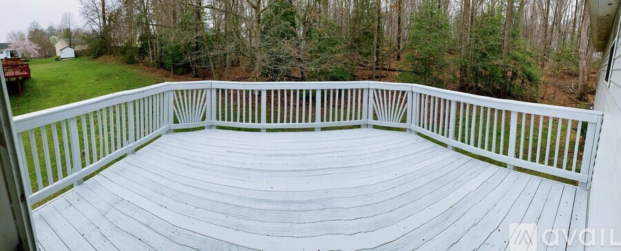 A white deck with a railing overlooks a wooded area.