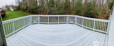 A white deck with a railing overlooks a wooded area.