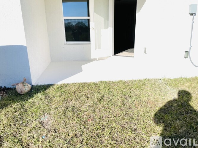 A shadow of a person is cast on a grassy area in front of a white building.