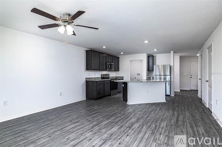 A spacious kitchen and living room with a ceiling fan and hardwood floors.