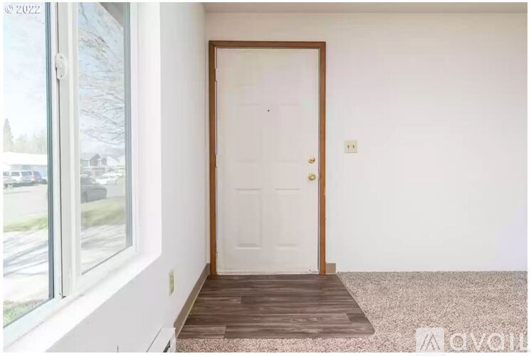 A white door with a wooden frame is in the middle of a room with a window on the left.