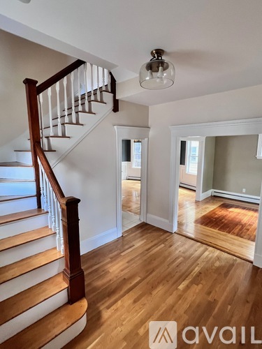 A wooden staircase with a white railing leads up to a landing with a chandelier and a doorway.