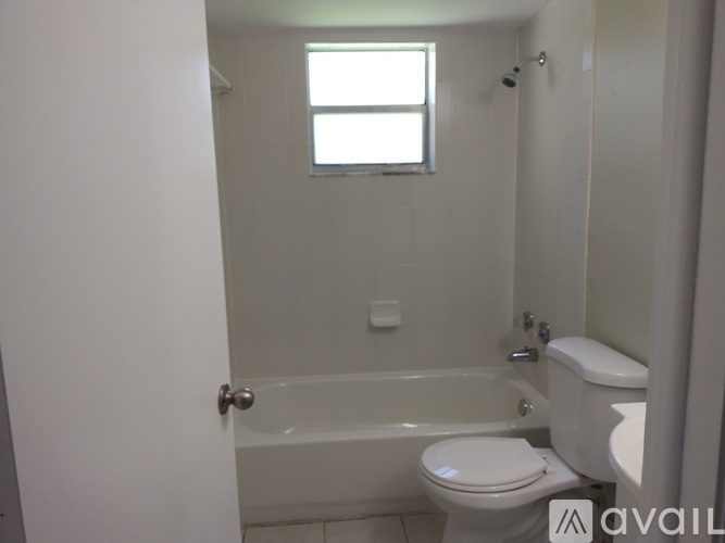 A white bathroom with a toilet, tub, and window.