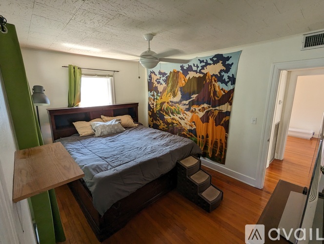 A bedroom with a bed, a fan, and a mountain mural on the wall.