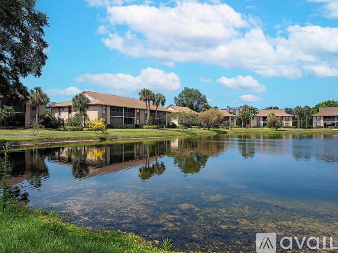A serene landscape with a lake, buildings, and trees under a clear sky.