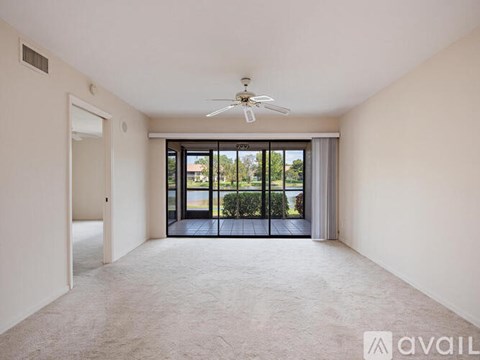 A spacious room with a ceiling fan and sliding glass doors leading to a balcony.