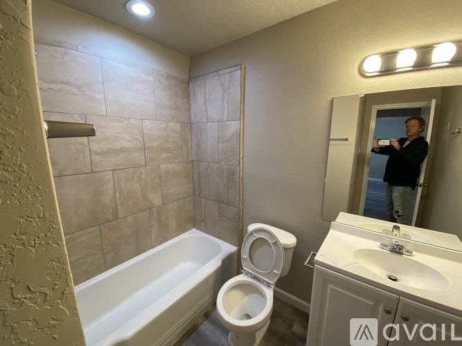 A man is taking a picture of a bathroom with a toilet, sink, and bathtub.