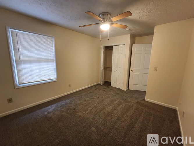 A room with a carpeted floor, a ceiling fan, and a window with blinds.