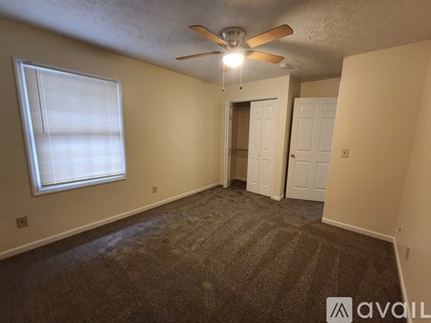 A room with a carpeted floor, a ceiling fan, and a window with blinds.