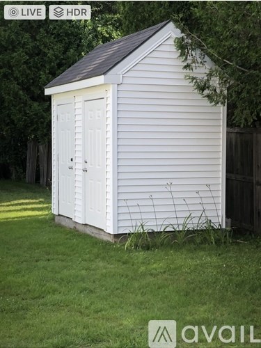 A small white shed with a black roof is situated in a grassy area.