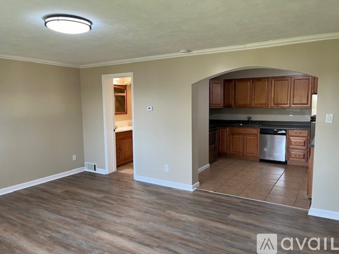A kitchen with wooden cabinets and a refrigerator is visible through an archway.