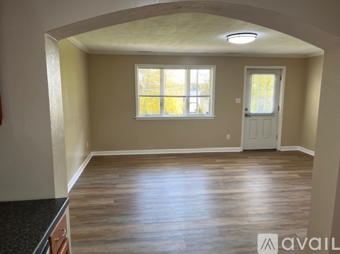 A room with a white door and a window with a view of trees.